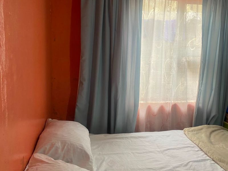 A bedroom featuring orange walls and a window with curtain rails, requiring cosmetic updates to improve the overall finish and aesthetic appeal.