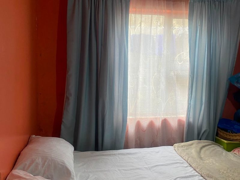 A bedroom featuring a window with curtains and a ventilation grille, requiring cosmetic updates to the wall finishes and ceiling.