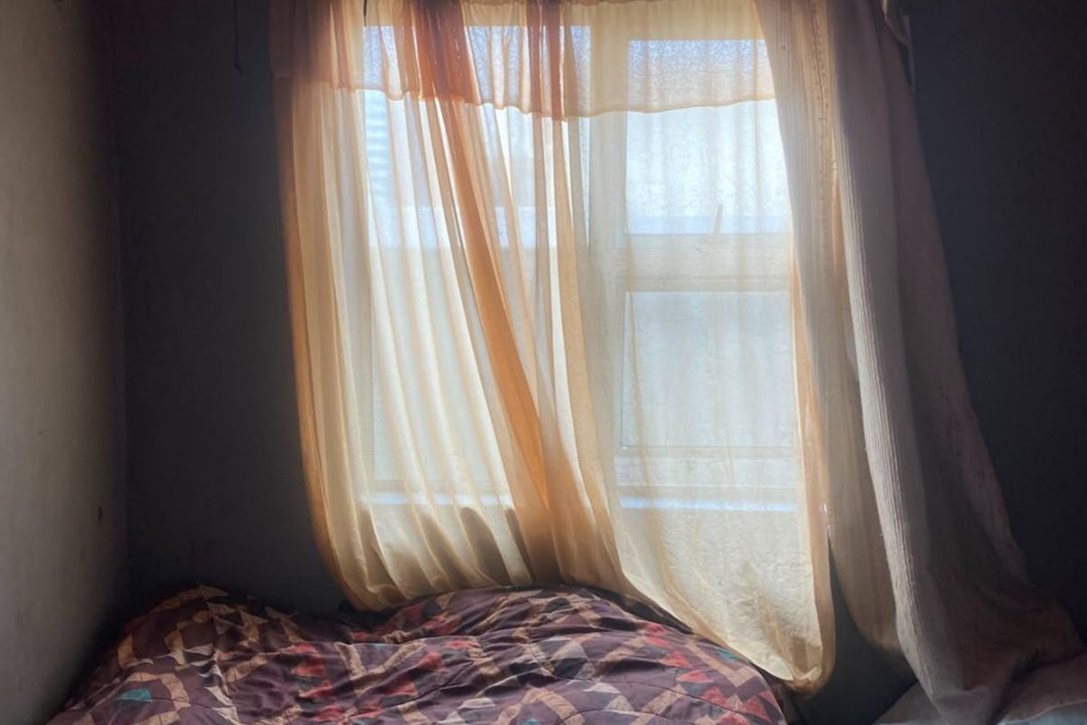 A bedroom featuring a window with ventilation brick and unfinished wall and ceiling surfaces, requiring cosmetic updates and repairs.