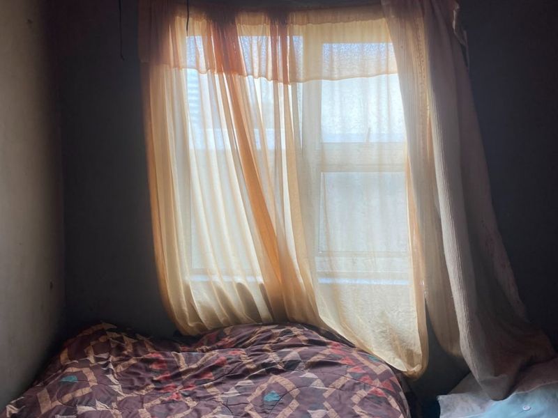 A bedroom featuring a window with ventilation brick and unfinished wall and ceiling surfaces, requiring cosmetic updates and repairs.