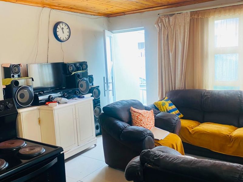 Open plan living area featuring tiled flooring and a timber tongue and groove ceiling, with an integrated stove and direct access to the exterior.