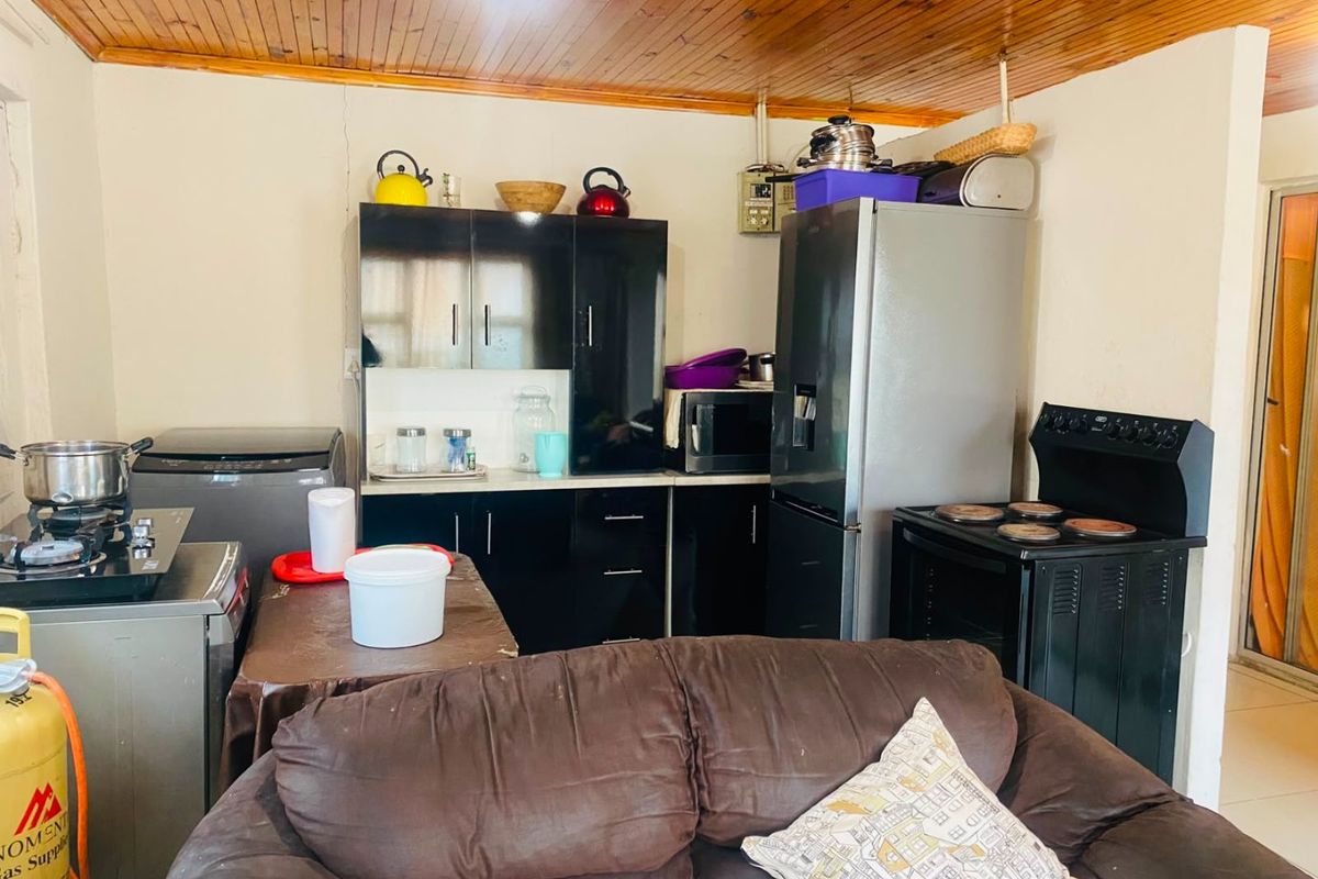 A compact kitchen area featuring dark cabinetry, a freestanding stove, and a timber-paneled ceiling, requiring some cosmetic updates to improve the overall aesthetic.