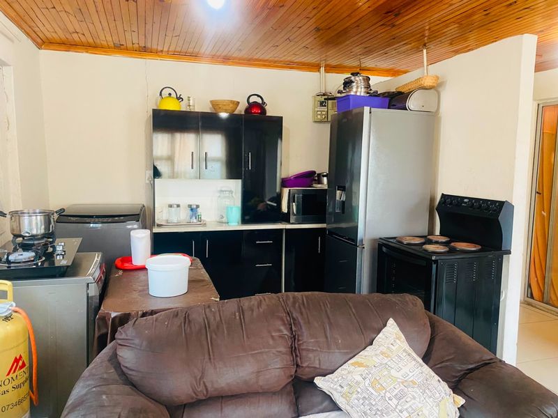 A compact kitchen area featuring dark cabinetry, a freestanding stove, and a timber-paneled ceiling, requiring some cosmetic updates to improve the overall aesthetic.