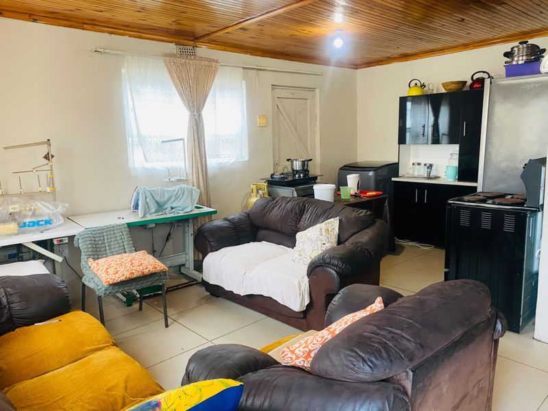 Open plan living area featuring a timber ceiling, tiled floors, and a compact kitchen corner with built-in cabinetry and a freestanding stove.