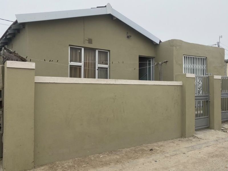 Front exterior view of a single-story house featuring a perimeter wall, metal security gate, and gabled roof structure.