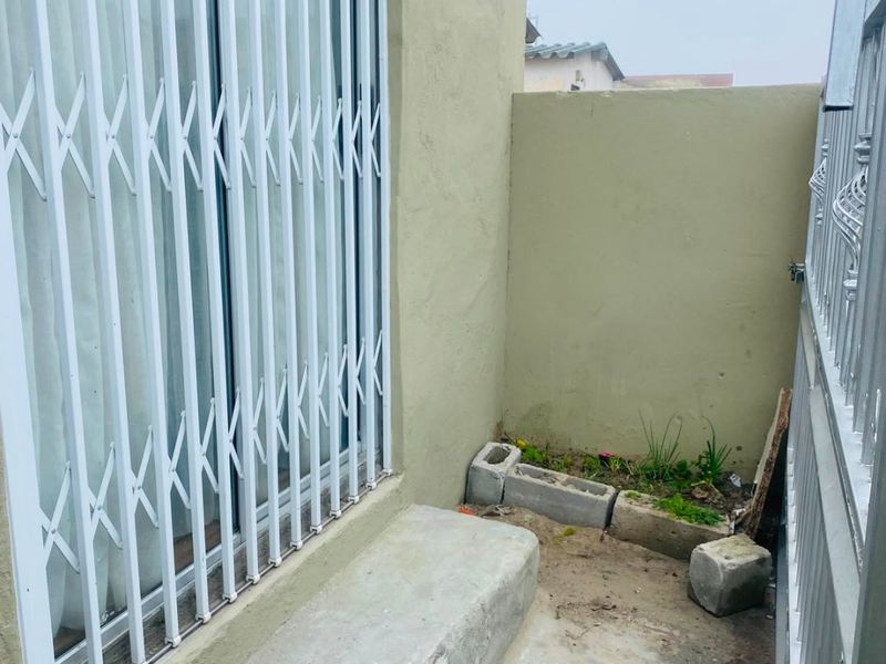 A small outdoor patio area featuring a concrete step, security gate, and boundary wall, requiring landscaping and surface finishing to improve its appeal.