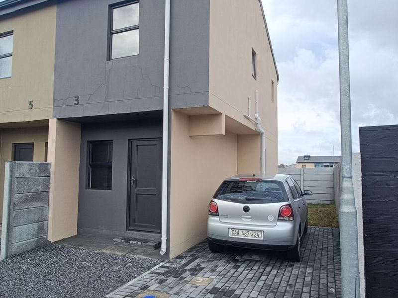 Front elevation of a two-story townhouse featuring a paved driveway, neutral exterior paint, and a precast concrete boundary wall.