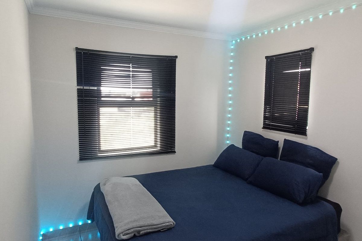 A compact bedroom featuring tiled flooring, coving, and two windows fitted with dark venetian blinds.