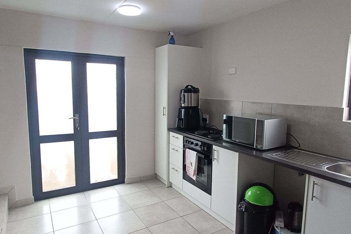 A functional kitchen area featuring built-in cabinetry, a stainless steel sink, integrated oven and hob, tiled flooring, and direct access via double doors.