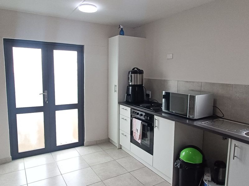 A functional kitchen area featuring built-in cabinetry, a stainless steel sink, integrated oven and hob, tiled flooring, and direct access via double doors.