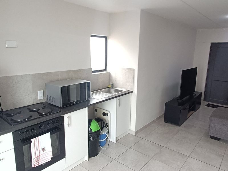 Open-plan living area featuring a compact kitchen with built-in cabinetry, electric hob, oven, and tiled flooring throughout the combined space.