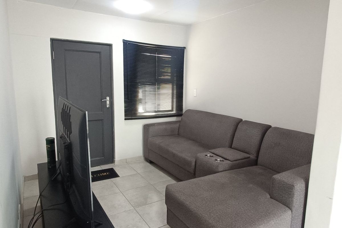A compact living room featuring tiled flooring, a window with venetian blinds, and a neutral wall finish.