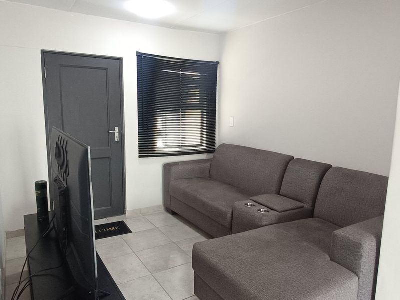 A compact living room featuring tiled flooring, a window with venetian blinds, and a neutral wall finish.