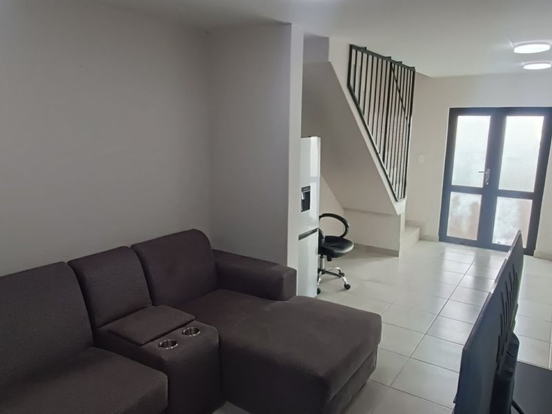 Open plan living area featuring tiled flooring, a staircase with a metal balustrade, and access to the exterior through double glass doors.