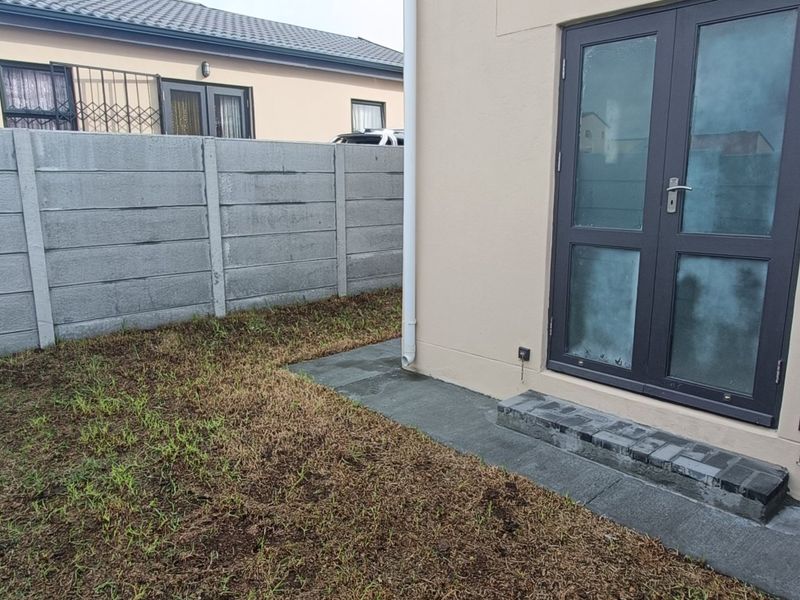 Rear exterior view of the townhouse featuring a paved step, double glass doors, and a private garden area enclosed by a precast concrete wall.