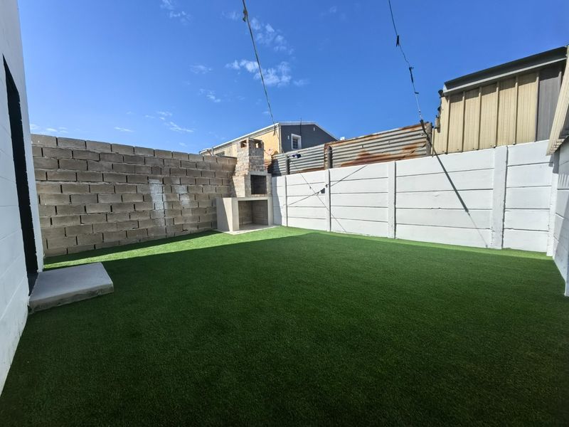 A private rear courtyard featuring artificial grass, a built-in braai, and secure boundary walls, offering a low-maintenance outdoor entertainment space.