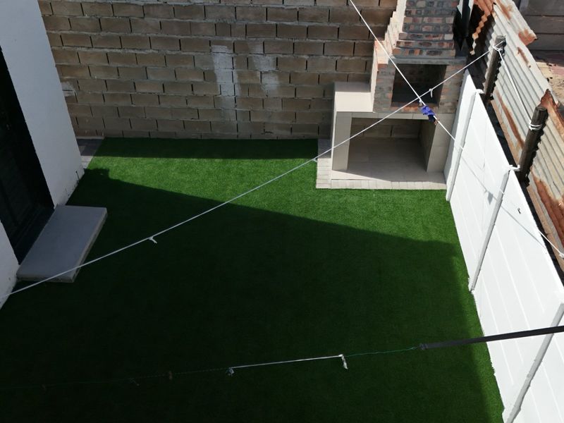 A compact rear courtyard featuring artificial grass, a built-in brick braai, and perimeter walling, offering a low-maintenance outdoor space.