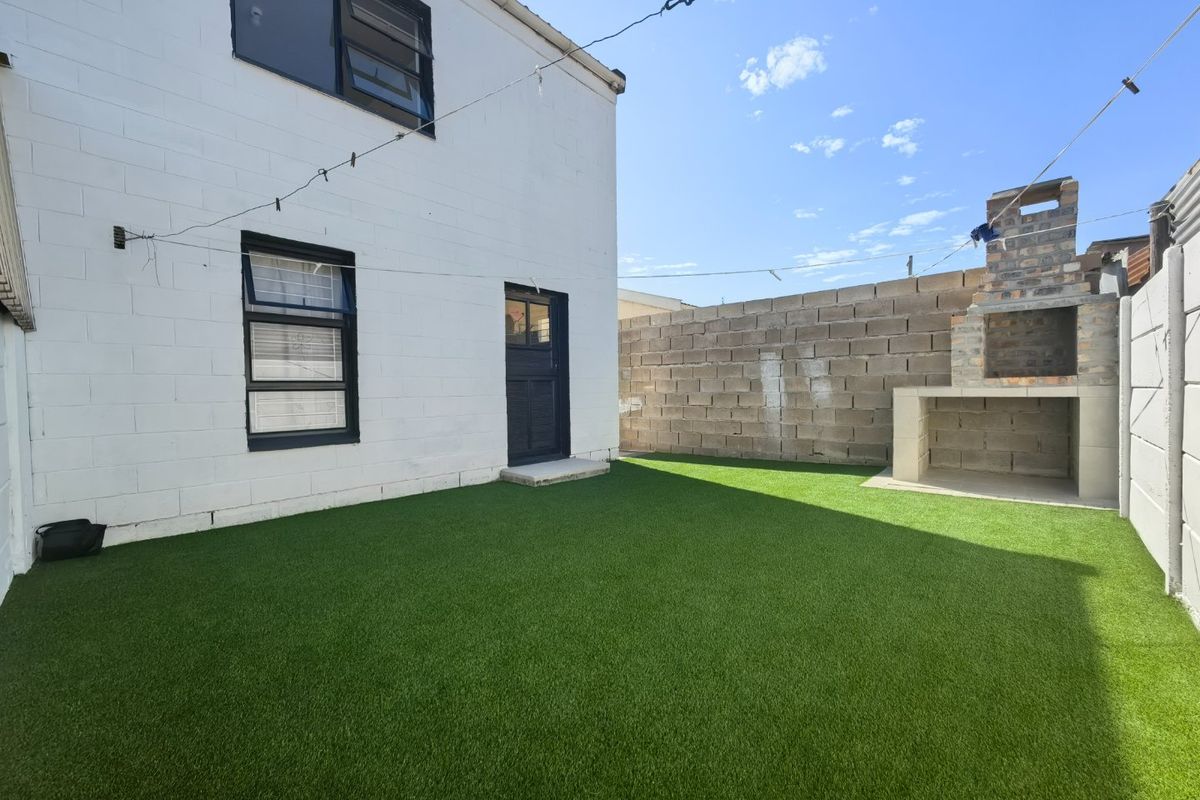 Rear courtyard featuring an artificial lawn, a built-in brick braai, and a painted masonry exterior wall.