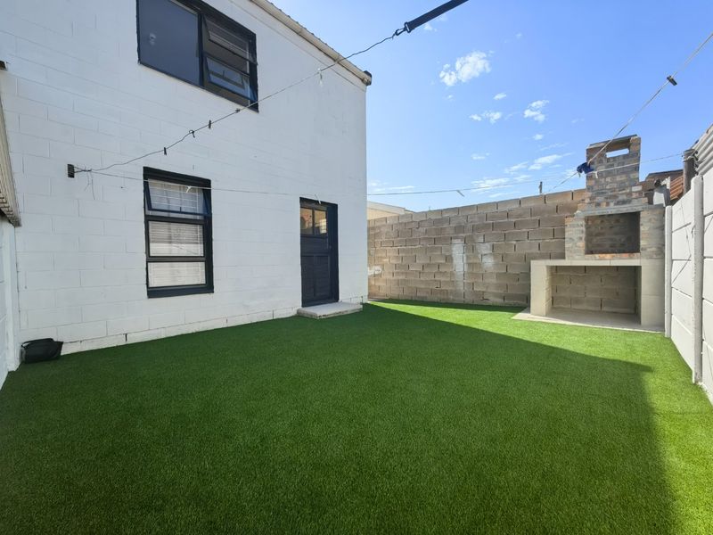 Rear courtyard featuring an artificial lawn, a built-in brick braai, and a painted masonry exterior wall.