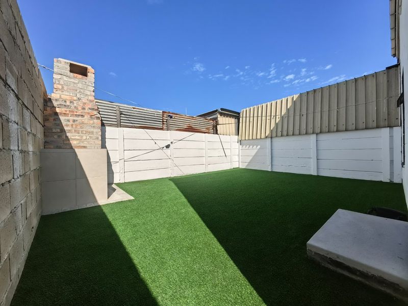 A private rear courtyard featuring artificial turf, a built-in brick fireplace, and secure perimeter walling.