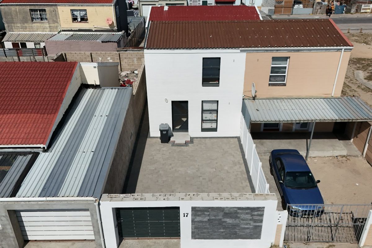 Aerial view of a residential property featuring a paved driveway, secure boundary wall with gate, and a covered carport area.