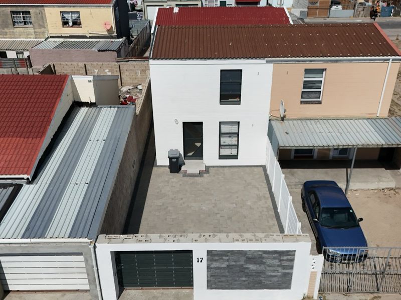 Aerial view of a residential property featuring a paved driveway, secure boundary wall with gate, and a covered carport area.