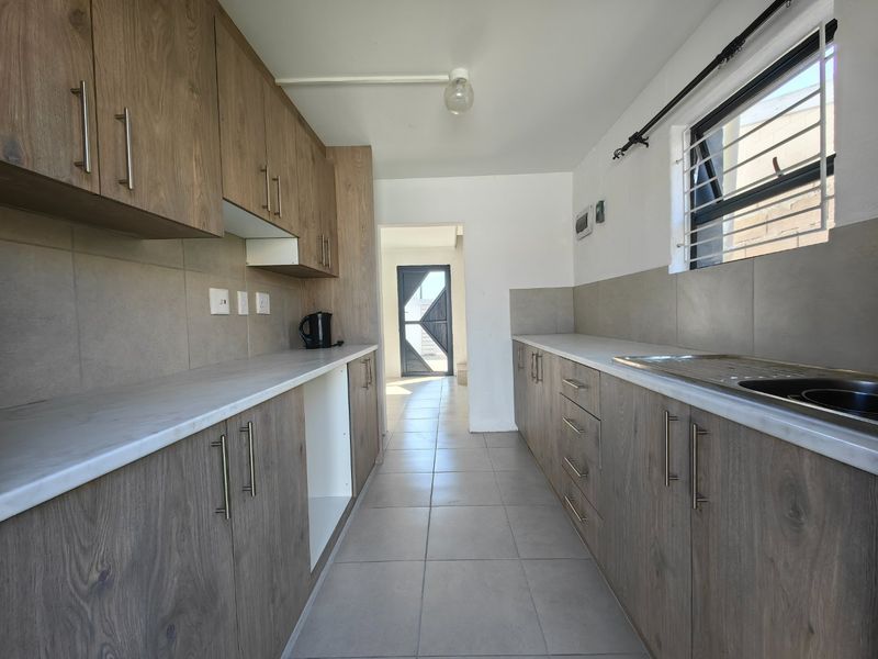 A clean, galley-style kitchen featuring wood-look cabinetry, neutral countertops, tiled splashbacks, and tiled flooring, offering a functional and well-maintained workspace.
