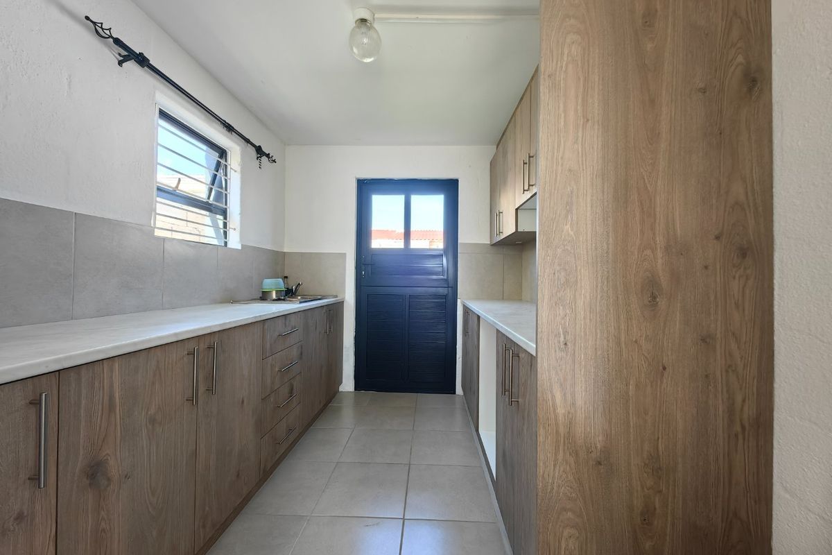 A clean, galley-style kitchen featuring modern wood-look cabinetry, neutral tiled flooring, and a functional layout with direct exterior access.
