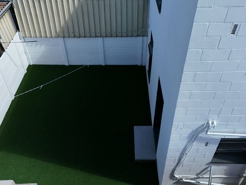 An elevated view of a compact rear courtyard featuring artificial turf, enclosed by white precast concrete boundary walls and the main building structure.