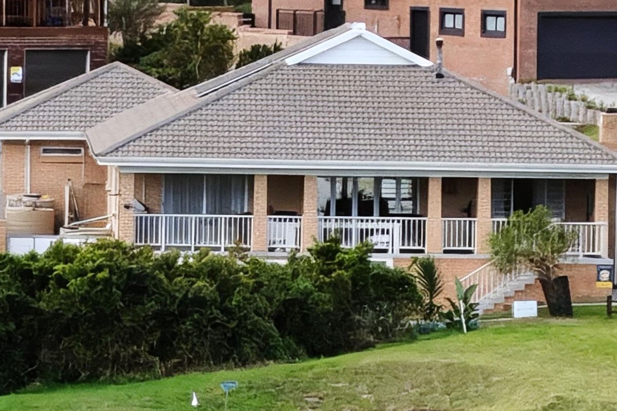 Rear view of a brick house featuring a covered patio with white railings and a tiled roof.