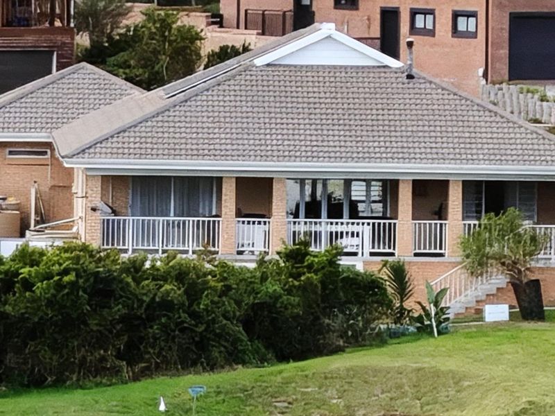 Rear view of a brick house featuring a covered patio with white railings and a tiled roof.