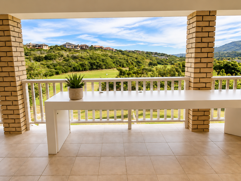 A covered balcony featuring brick columns, tiled flooring, and a white balustrade, offering expansive views of the surrounding landscape and golf course.