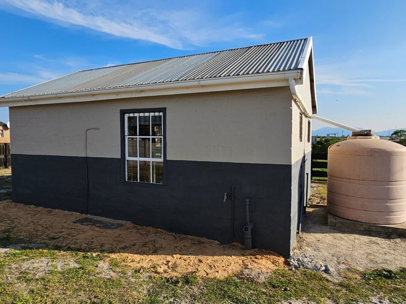 Rear view of the property featuring a painted exterior, corrugated metal roof, and an integrated water storage tank.