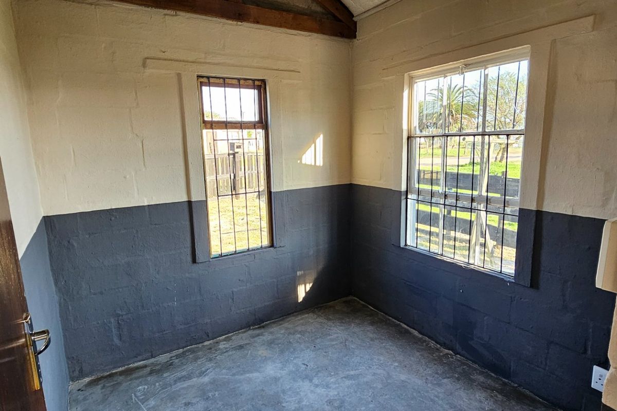 A small, empty room featuring exposed timber rafters, concrete flooring, and security bars on the windows, offering a blank canvas for renovation.