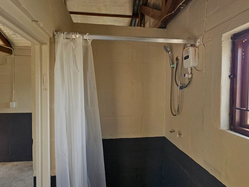 A basic bathroom area featuring an electric shower unit, exposed timber roof trusses, and painted blockwork walls.