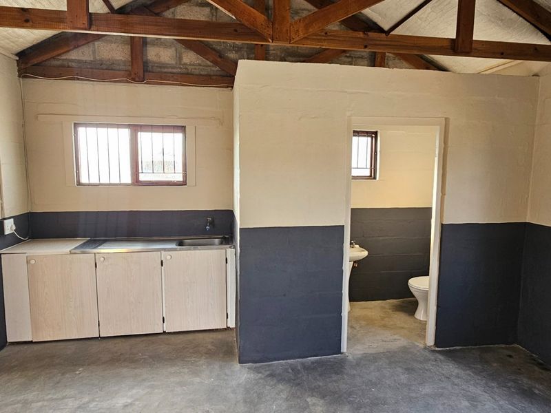 A functional utility space featuring exposed timber trusses, concrete block walls, a basic kitchenette area, and an adjoining small bathroom with a toilet and basin.
