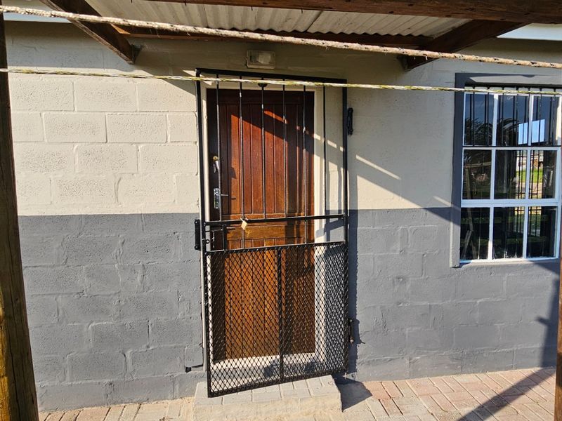 Rear exterior view featuring a paved patio area, timber pergola, and a secure entrance with a metal security gate and timber door.
