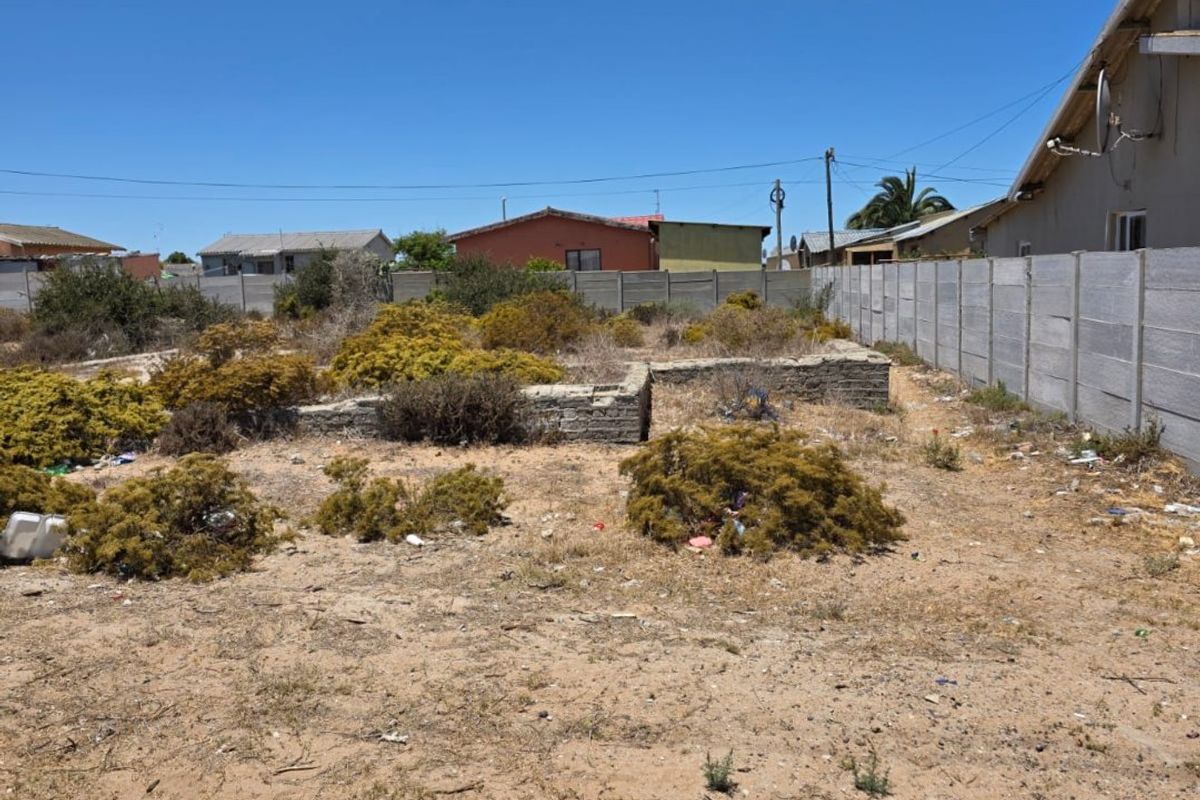 Vacant residential plot featuring a precast concrete boundary wall and stone foundation remnants, requiring clearing and site preparation.