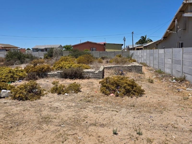 Vacant residential plot featuring a precast concrete boundary wall and stone foundation remnants, requiring clearing and site preparation.