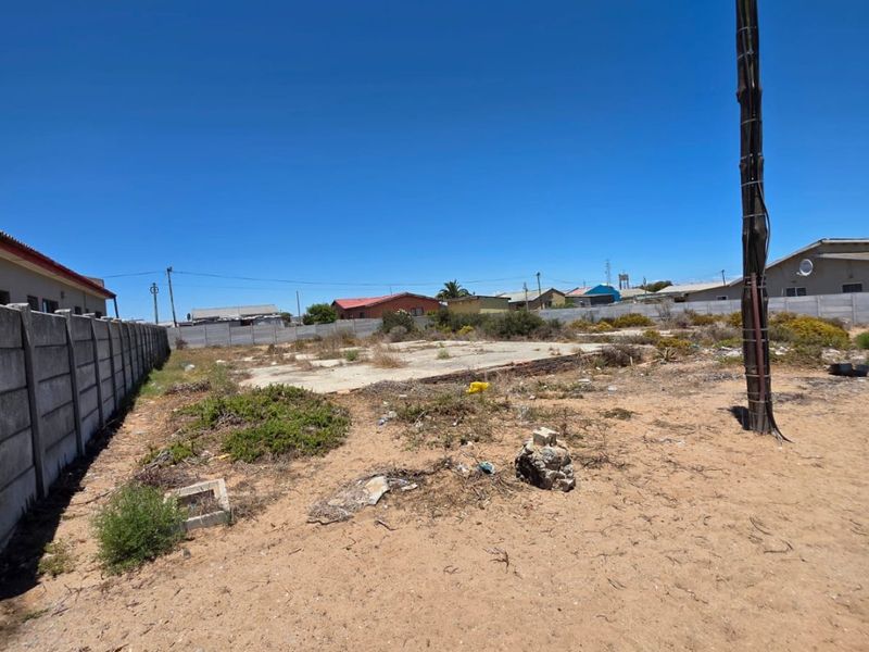 Vacant residential plot featuring a concrete slab foundation, enclosed by precast concrete boundary walls, with surrounding vegetation and utility infrastructure.