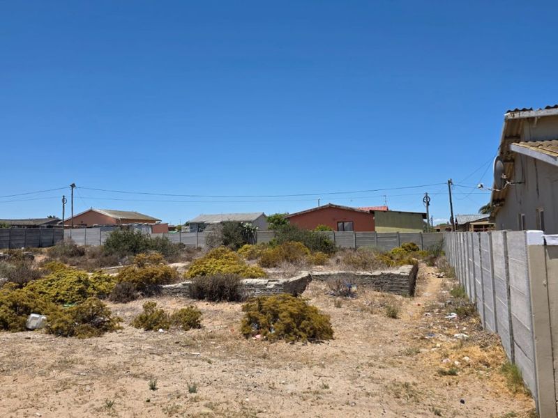 A vacant residential plot featuring a precast concrete boundary wall and natural ground cover, ready for development.