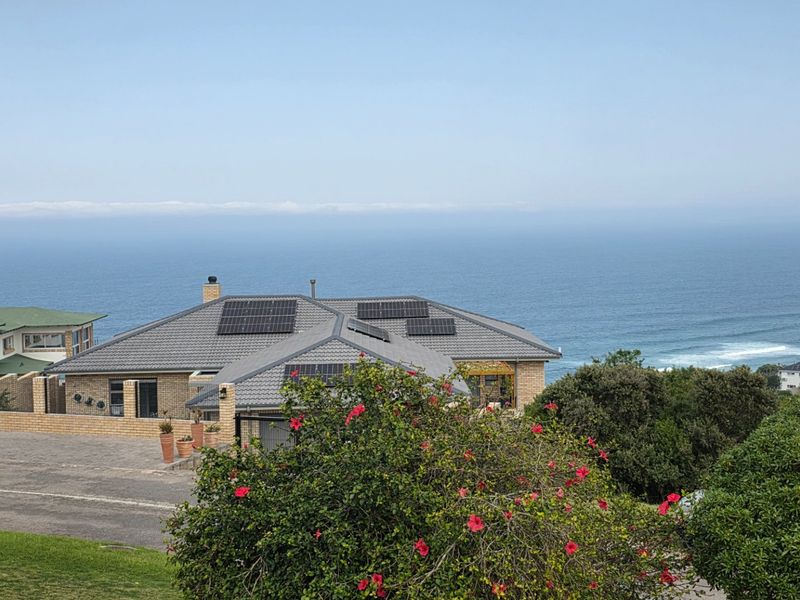An elevated view of a residential property featuring a tiled roof with integrated solar panels, overlooking the ocean.