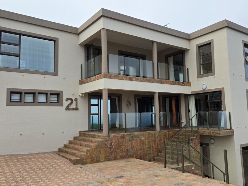 Modern multi-story residential facade featuring stone cladding, glass balustrades, and a paved driveway entrance.
