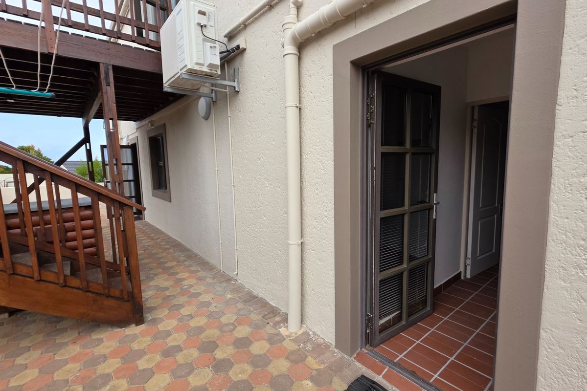 Rear exterior view featuring a paved patio area, timber staircase, and access to the interior through a glazed door.