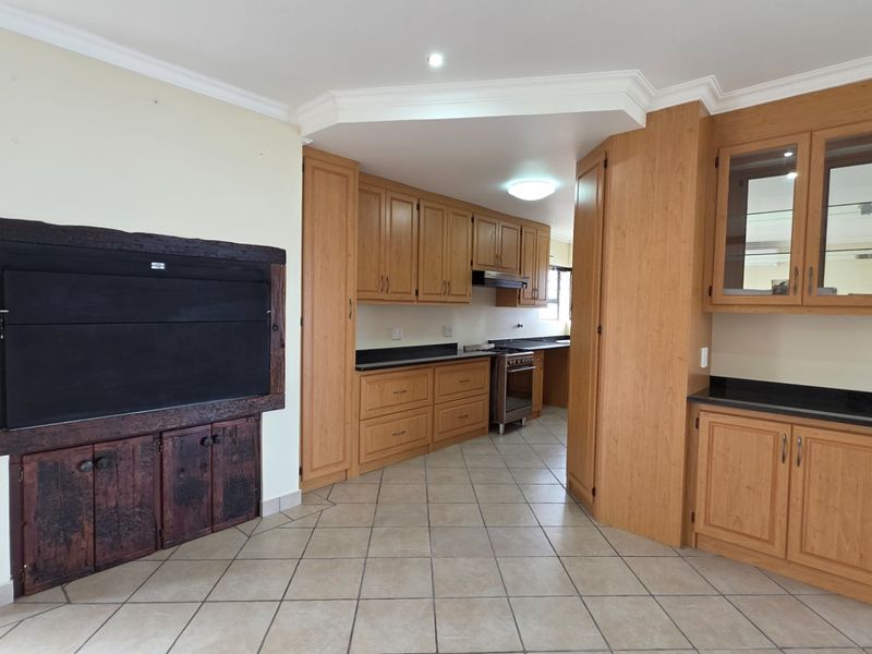 Spacious open-plan kitchen and living area featuring extensive wooden cabinetry, granite countertops, a built-in fireplace, and neutral tiled flooring throughout.
