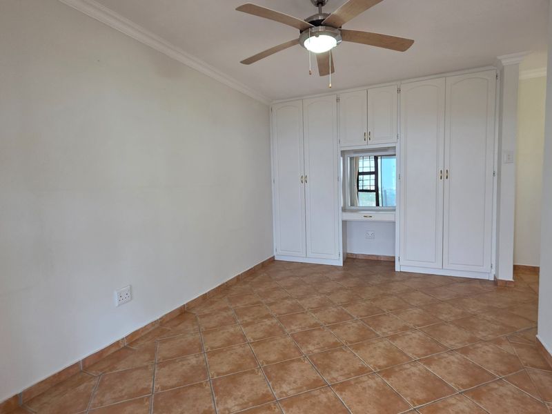 Spacious bedroom featuring neutral walls, tiled flooring, a ceiling fan, and extensive built-in cupboard storage with an integrated vanity section.