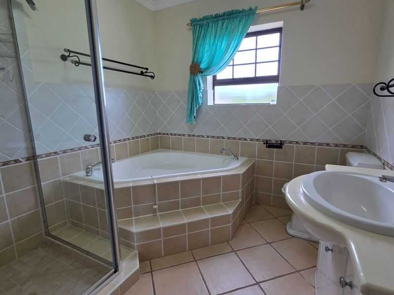 A functional bathroom featuring a corner bathtub, separate glass-enclosed shower, and a vanity basin with tiled finishes throughout.