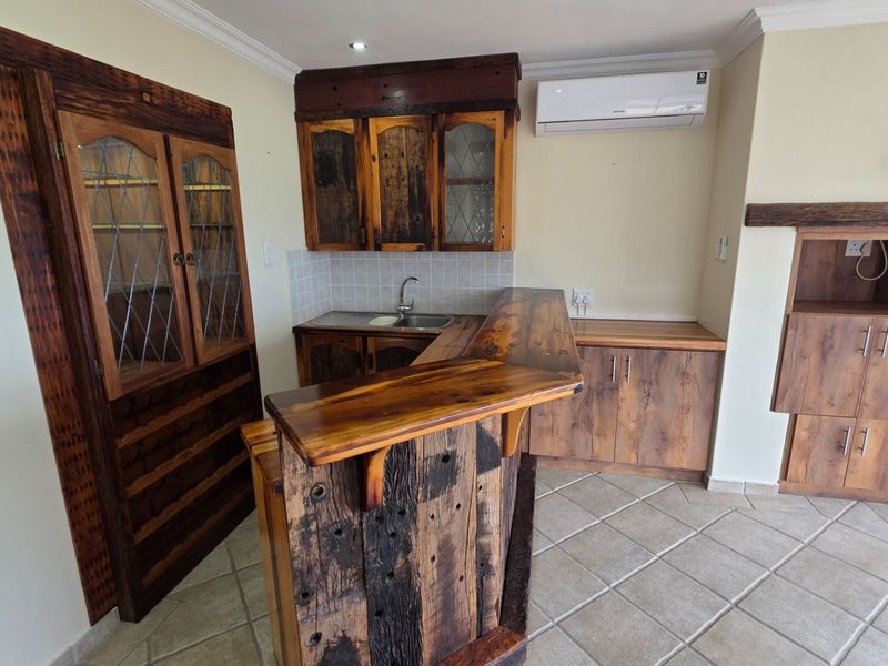 A rustic-style kitchen featuring custom wooden cabinetry, a breakfast bar, tiled flooring, and a wall-mounted air conditioning unit.