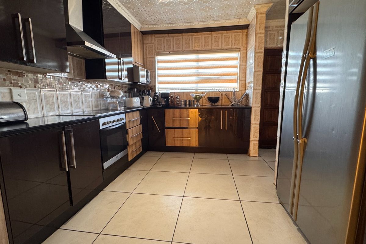 A functional kitchen featuring dark cabinetry, tiled backsplash, built-in oven, extractor fan, and tiled flooring with a decorative ceiling finish.