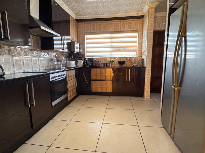 A functional kitchen featuring dark cabinetry, tiled backsplash, built-in oven, extractor fan, and tiled flooring with a decorative ceiling finish.